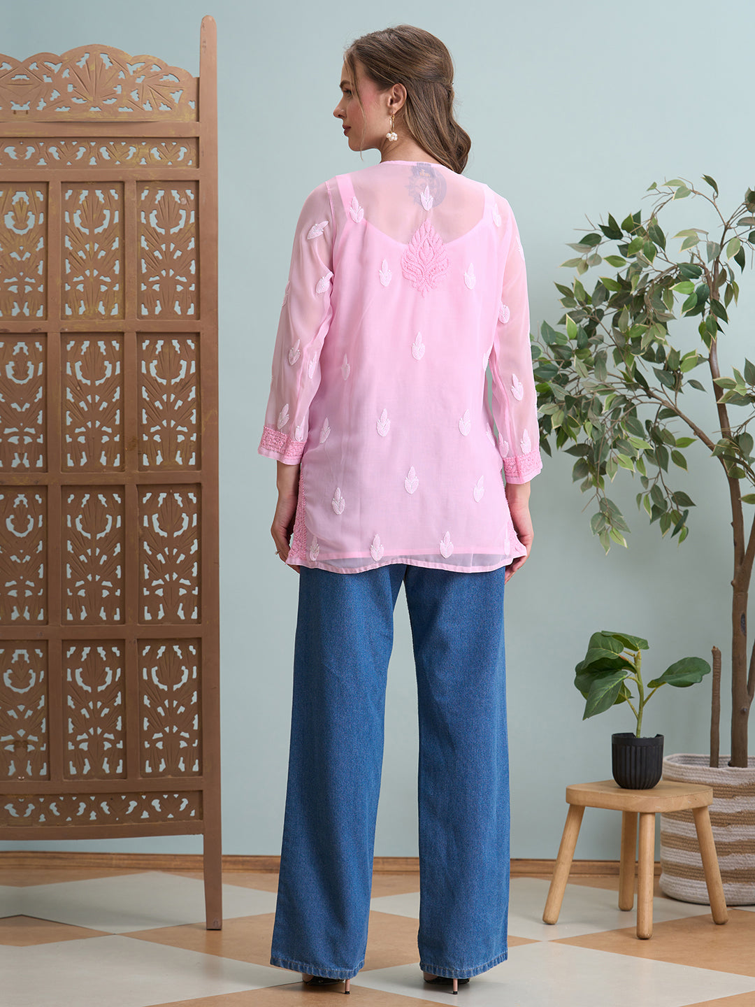 Woman wearing a pink top and blue pants standing in a room with decorative elements.