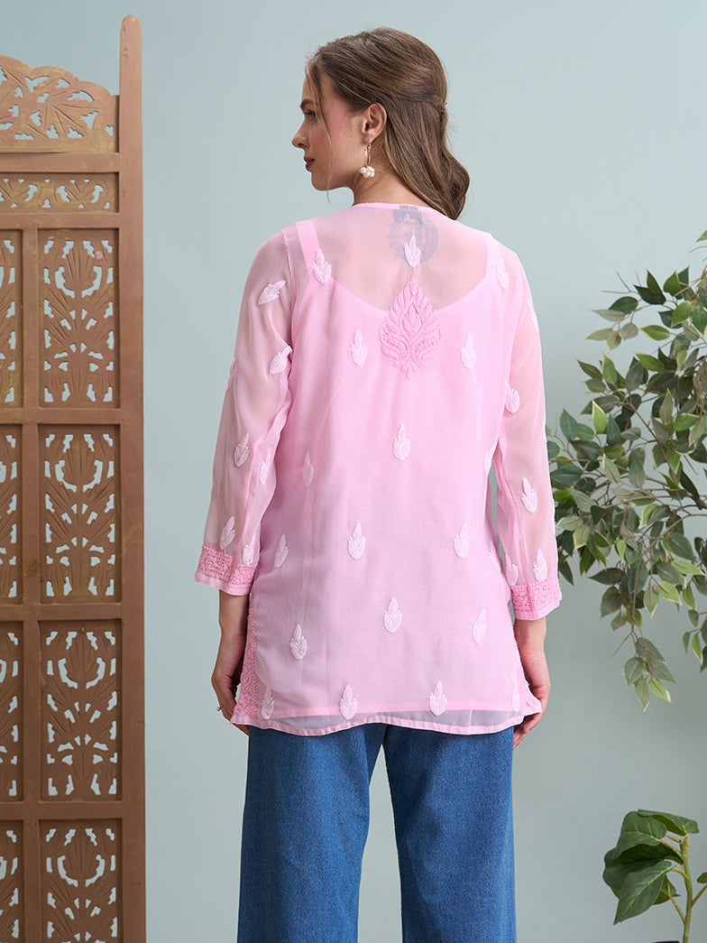 Woman wearing a pink top and blue pants standing in a room with decorative elements.