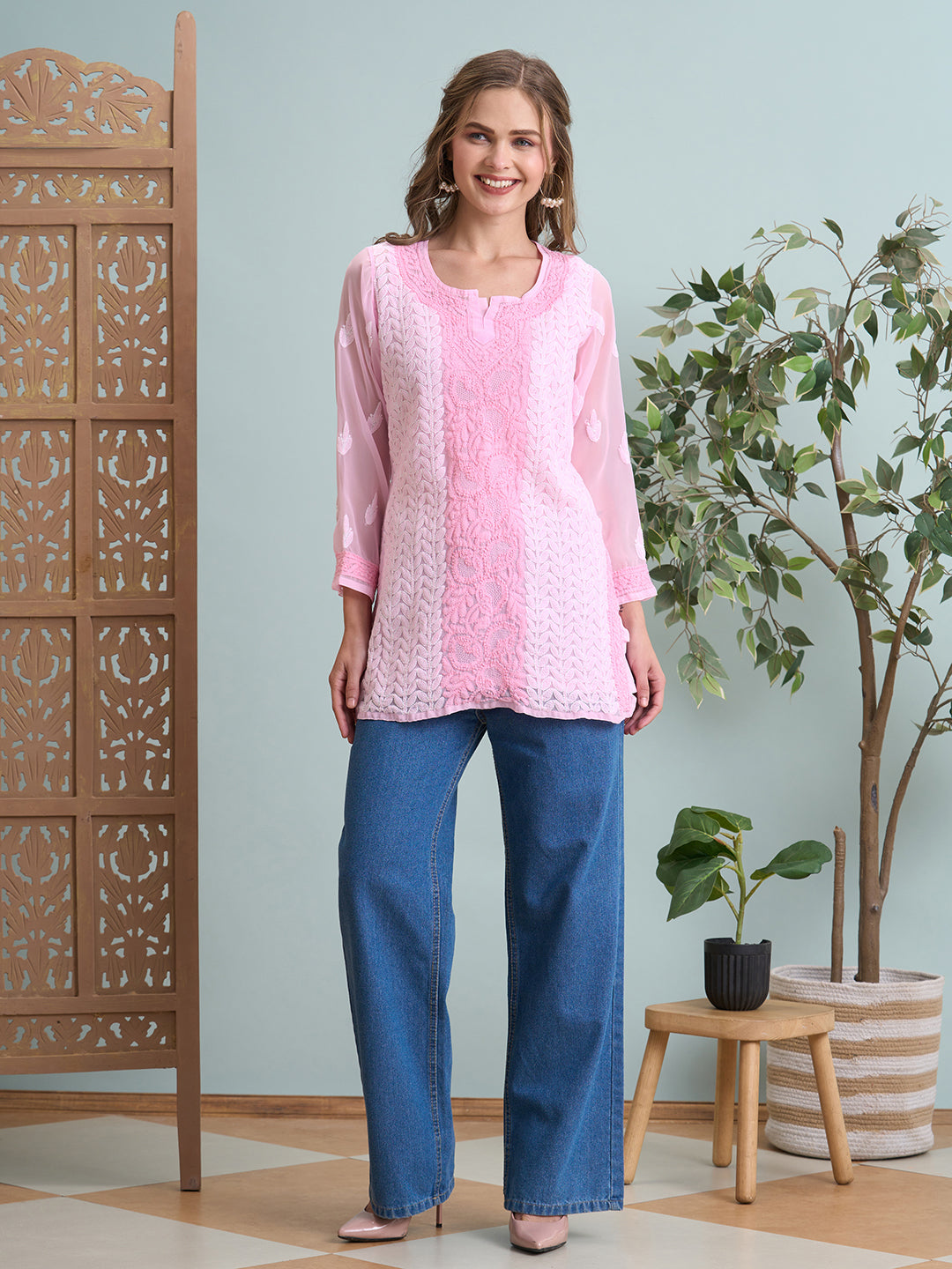 Woman wearing a pink top and blue jeans standing in a room with decorative elements.