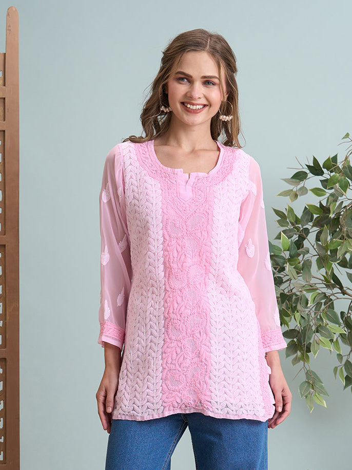 Woman wearing a pink top and blue jeans standing in a room with decorative elements.