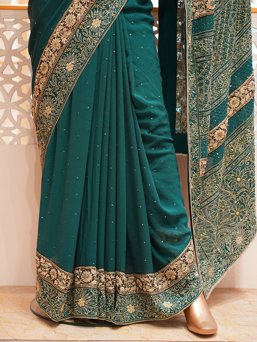 Green saree with gold embroidery on a wooden floor