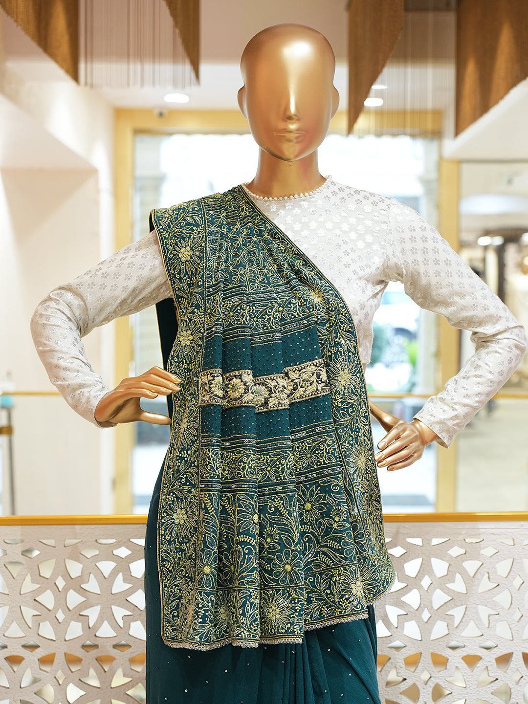 Mannequin wearing a traditional outfit with a green and gold patterned top and white sleeves.